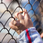 Immigrant child's hand on a grid of a metal fence