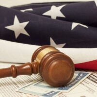 A wooden gavel resting on a newspaper, with an American flag in the background.